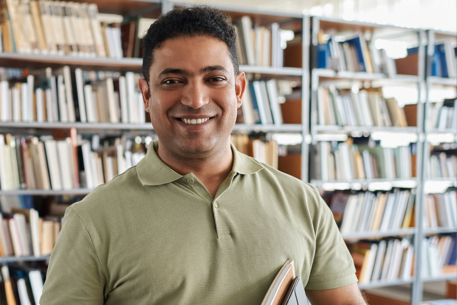 a smiling man holding a book in a library.