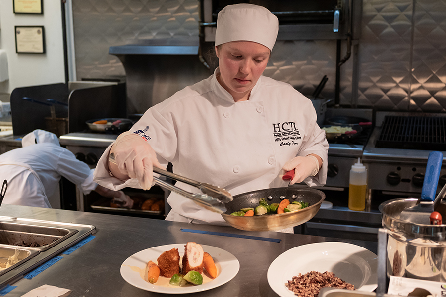 student putting food on plate in commercial kitchen