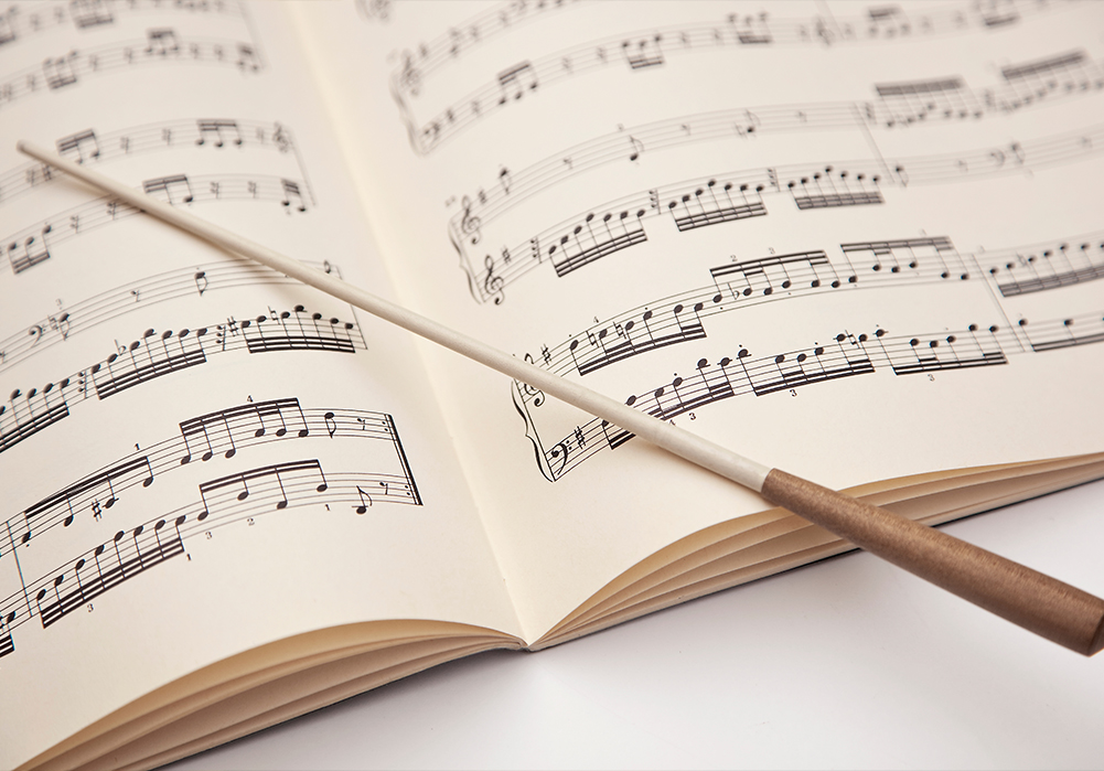 Close-up of a conductor's baton lying diagonally across open sheet music.
