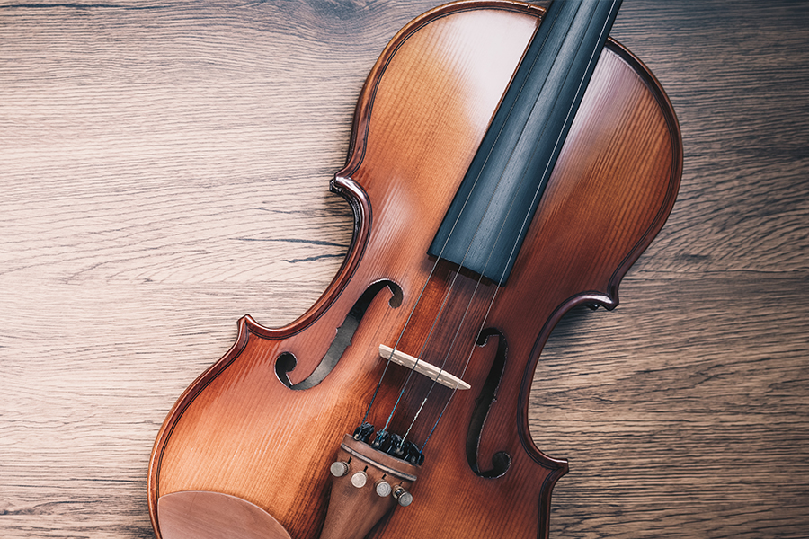 Close-up of a violin with its bow lying across the strings on a wooden surface.