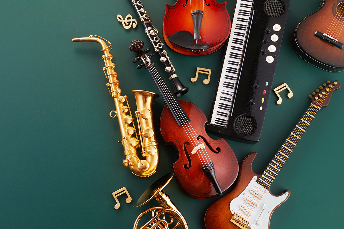 An assortment of musical instruments arranged on a green surface, including a saxophone, clarinet, violin, keyboard, electric guitar, acoustic guitar, and French horn, with decorative music note accents.
