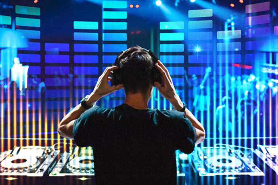 Rear view of a DJ wearing headphones performing in front of a bright digital audio equalizer display.