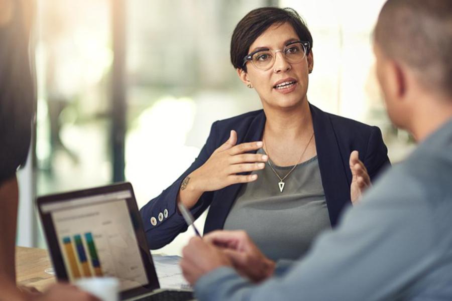 Professional woman with glasses and short hair gesturing during a business meeting with colleagues in a bright office.