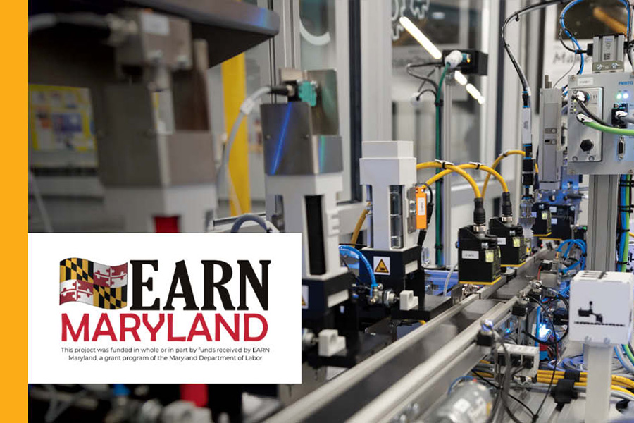 A close-up of industrial automation equipment with yellow and blue cables and electronic components, overlaid with the EARN Maryland logo and text noting the project was funded in whole or in part by the Maryland Department of Labor.