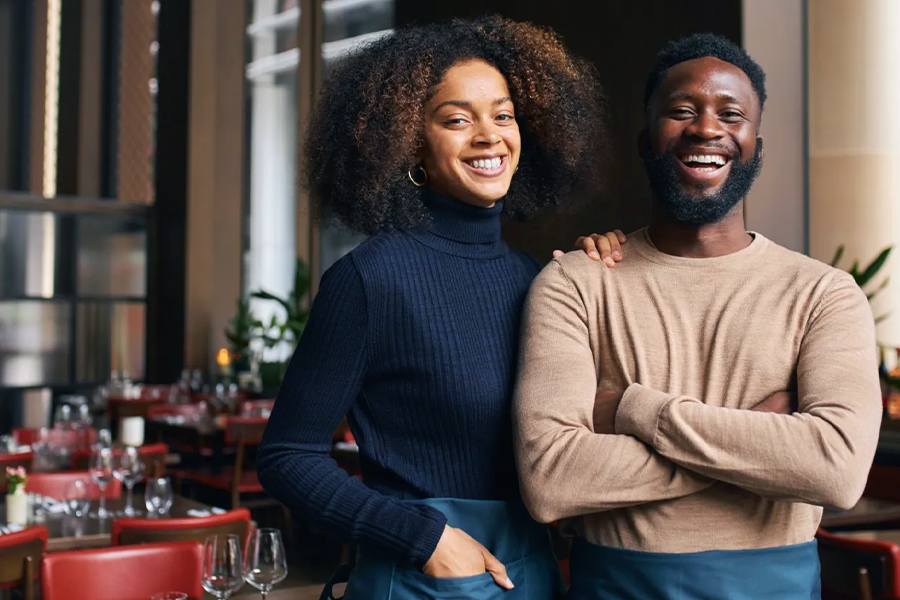 Two smiling restaurant owners standing together in a warmly lit dining room.