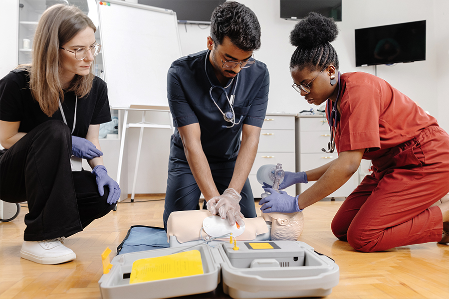 Healthcare students practicing CPR and AED skills on a training mannequin during a hands-on classroom session.