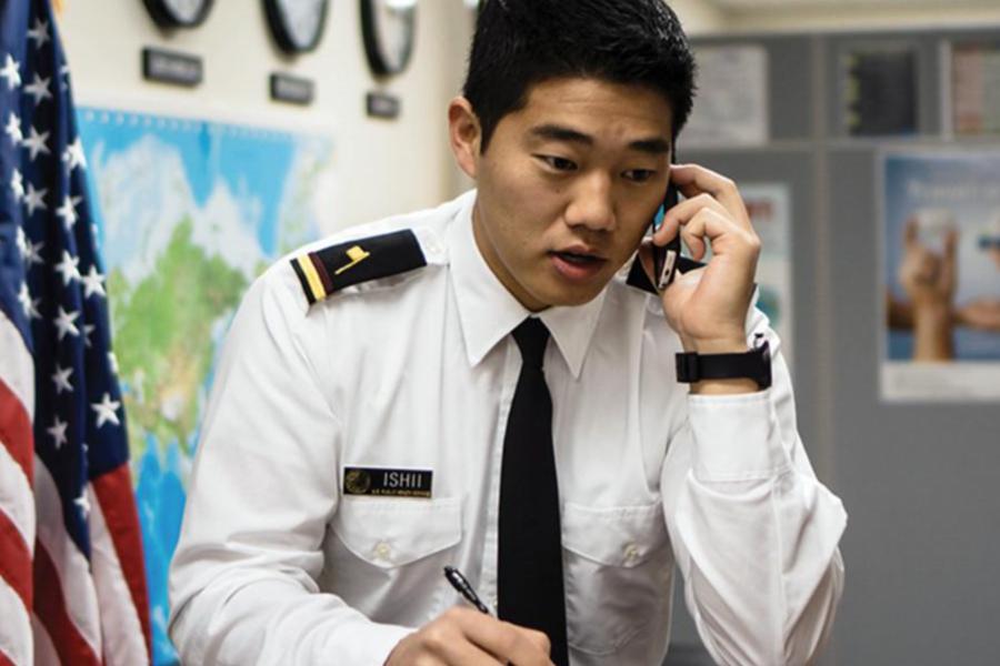 A man in a white dress uniform and black tie speaking on a mobile phone while taking notes.