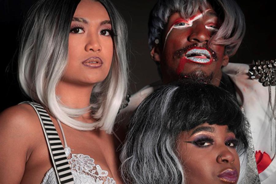 Three performers in elaborate theatrical makeup and silver wigs pose for a portrait, showcasing artistic costume design and stage makeup.