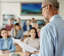 A professor lecturing to a classroom of students from a prepared document.