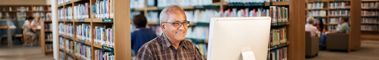An adult learner working on a computer in a bright library setting.