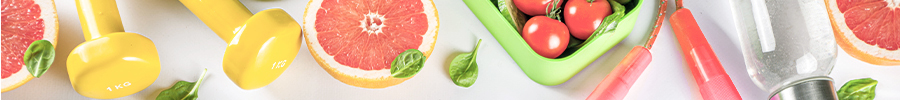 Top view of fitness and healthy living items including yellow dumbbells, grapefruit, leafy greens, cherry tomatoes, and a jump rope on a light background.