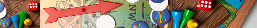 A close-up of a colorful board game showing a red arrow spinner, game tokens in blue, green, and yellow, circular game pieces with an anchor design, red dice, and an illustrated game board.